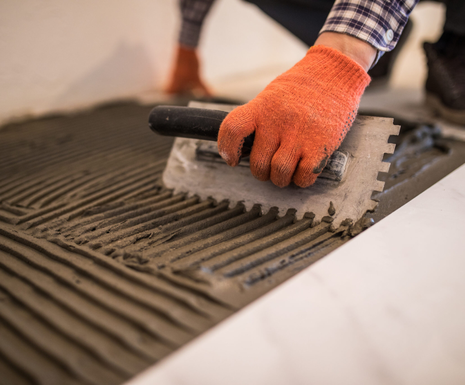 Troweling mortar onto a concrete floor in preparation for laying white floor tile.